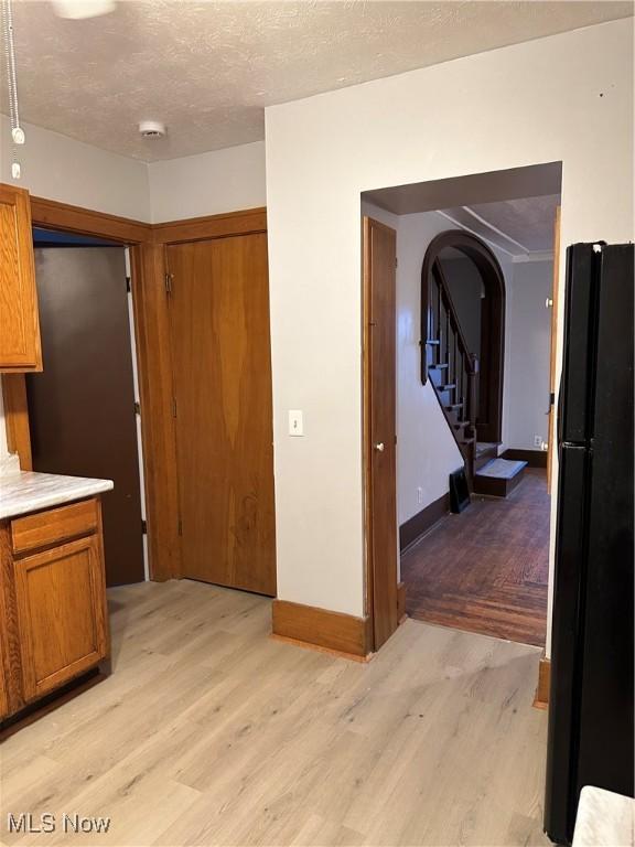 kitchen featuring arched walkways, light wood finished floors, light countertops, brown cabinetry, and freestanding refrigerator
