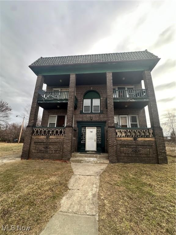 view of front of house with a balcony, brick siding, and a front yard