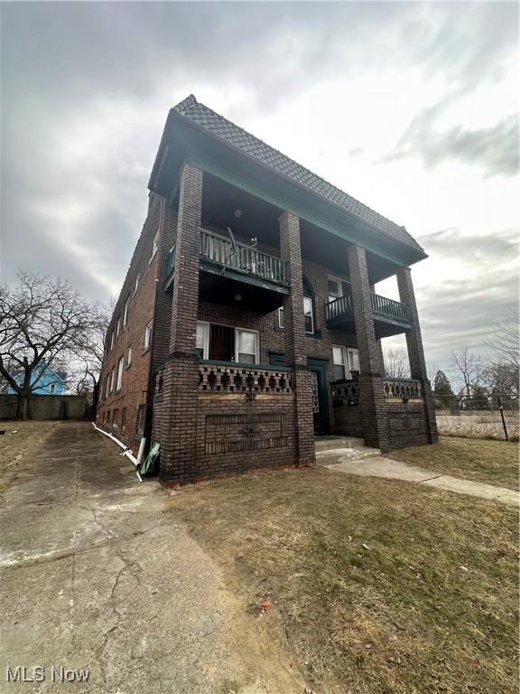 view of front of house featuring a front yard, brick siding, and a balcony