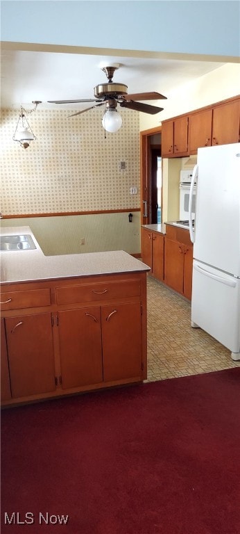 kitchen featuring light countertops, brown cabinetry, a ceiling fan, a sink, and white appliances