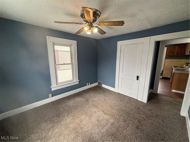 unfurnished bedroom with visible vents, dark carpet, a textured ceiling, and baseboards