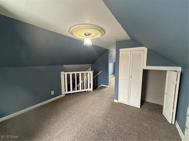 additional living space with dark colored carpet, lofted ceiling, and baseboards