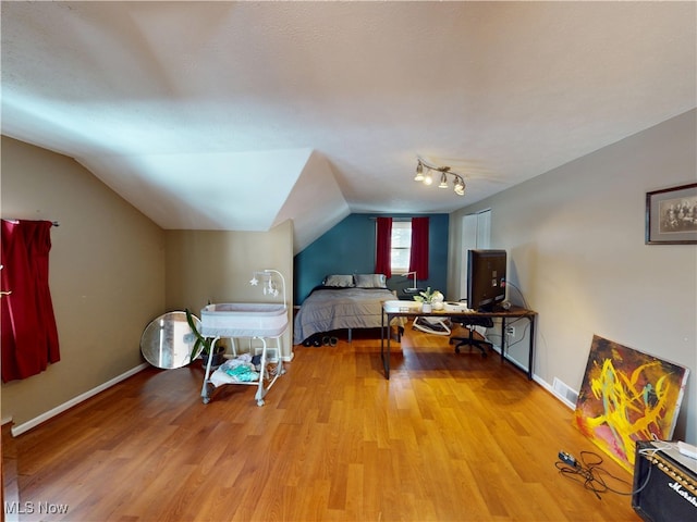 bedroom with lofted ceiling, wood finished floors, visible vents, and baseboards