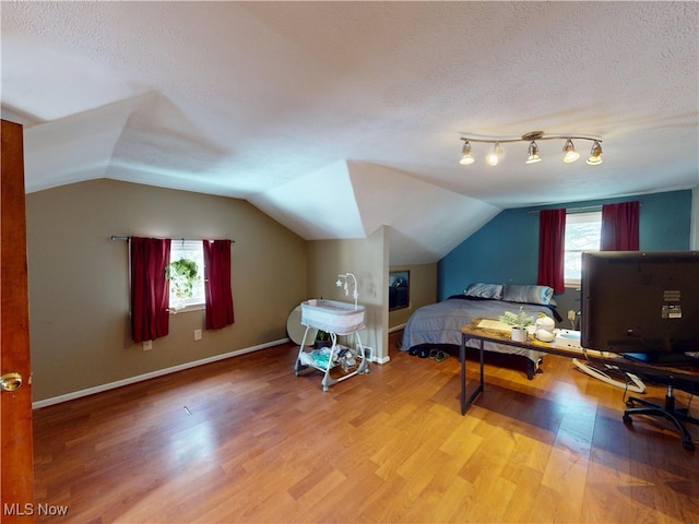 bedroom featuring lofted ceiling, a textured ceiling, baseboards, and wood finished floors