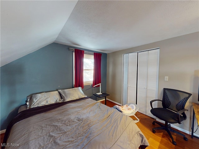 bedroom with a closet, vaulted ceiling, baseboards, and wood finished floors