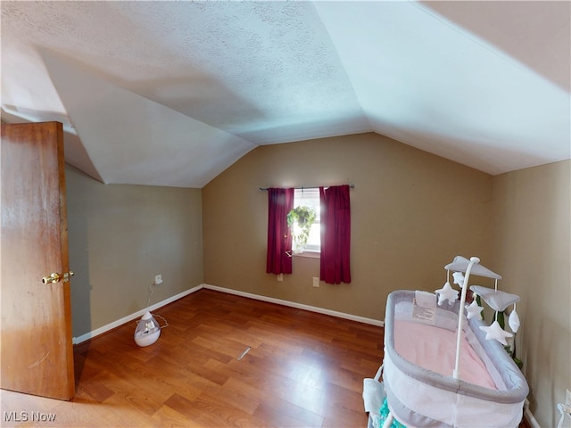 additional living space with vaulted ceiling, a textured ceiling, baseboards, and wood finished floors