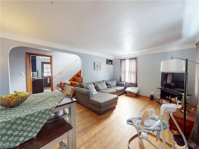 living room with arched walkways, light wood finished floors, stairway, and baseboards