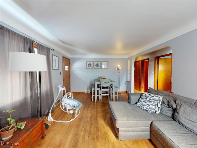 living room featuring arched walkways, light wood-type flooring, and baseboards