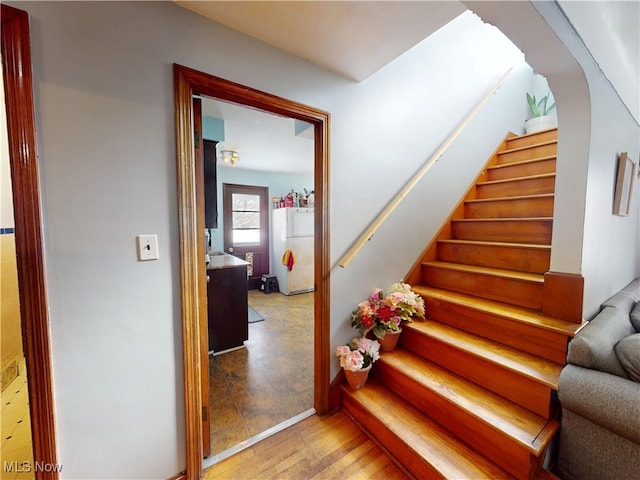 stairway featuring arched walkways and wood finished floors