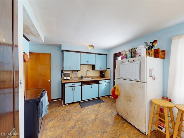 kitchen with decorative backsplash, dishwashing machine, freestanding refrigerator, light countertops, and a sink