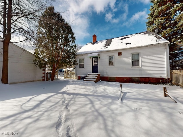 snow covered back of property featuring entry steps, fence, and a chimney