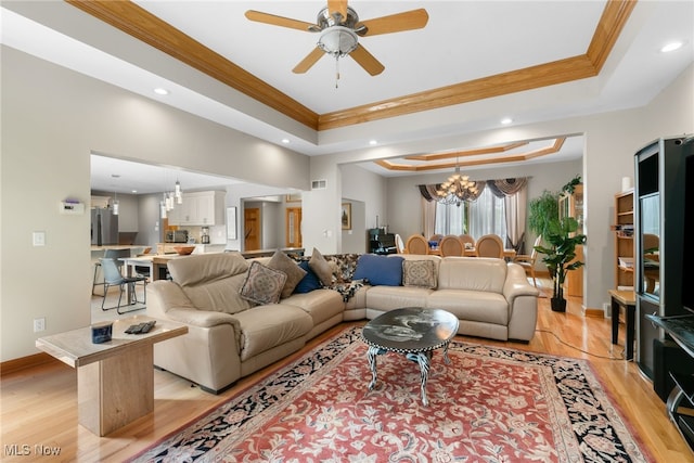 living room featuring light wood-style flooring, a tray ceiling, baseboards, and ornamental molding