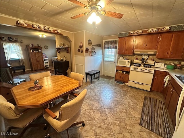 kitchen with under cabinet range hood, white appliances, a ceiling fan, light countertops, and wainscoting