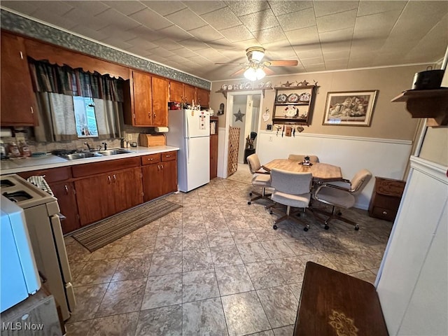 kitchen featuring white appliances, a sink, a ceiling fan, light countertops, and brown cabinetry