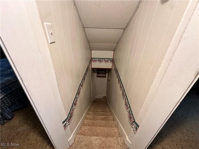 staircase featuring wood walls, carpet, and a drop ceiling