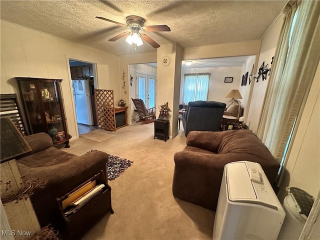 living area featuring light carpet, ceiling fan, and a textured ceiling