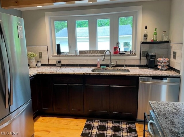 kitchen with light stone counters, stainless steel appliances, decorative backsplash, dark brown cabinetry, and a sink