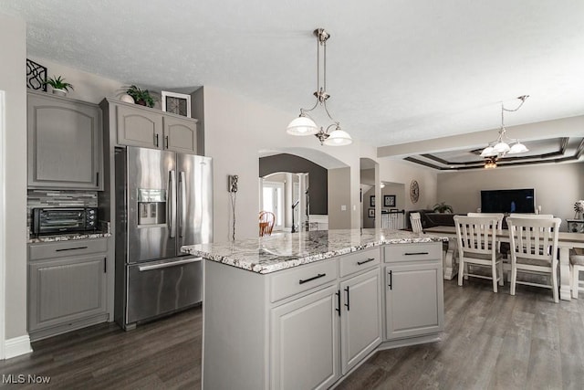 kitchen with arched walkways, a kitchen island, open floor plan, gray cabinets, and stainless steel fridge with ice dispenser