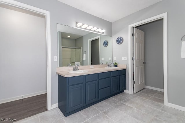 bathroom featuring double vanity, a stall shower, baseboards, and a sink