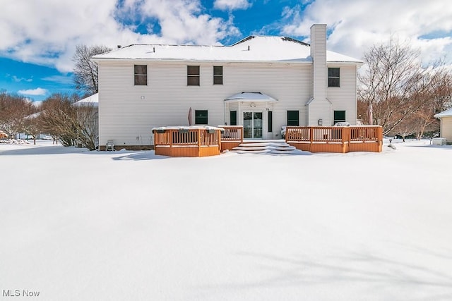 snow covered back of property with a chimney and a wooden deck