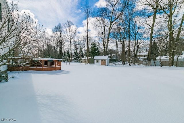 yard layered in snow featuring a storage shed, an outbuilding, and a wooden deck