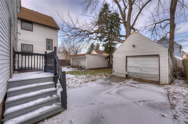 yard layered in snow featuring a garage, an outbuilding, and driveway