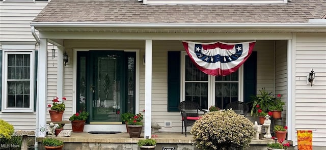 doorway to property featuring covered porch and roof with shingles