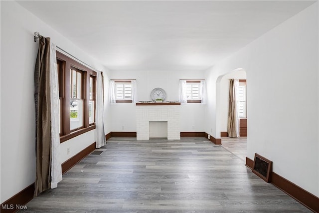 empty room featuring baseboards, visible vents, arched walkways, wood finished floors, and a fireplace