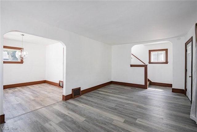 unfurnished room with baseboards, visible vents, arched walkways, dark wood-type flooring, and a healthy amount of sunlight