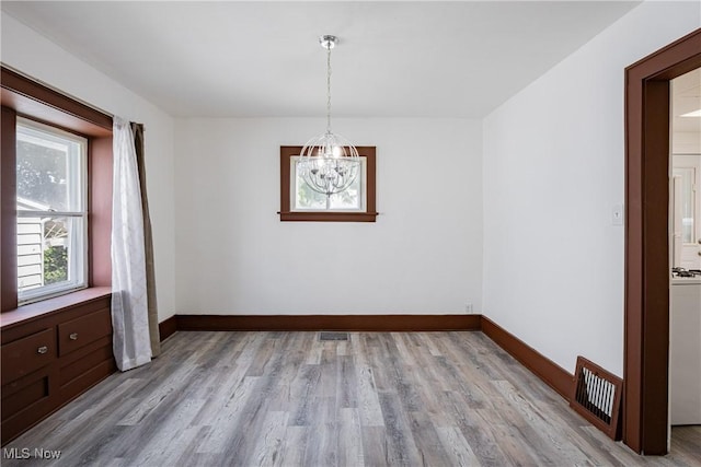 unfurnished dining area featuring a chandelier, light wood-style flooring, and baseboards