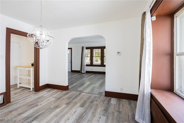 unfurnished dining area with arched walkways, light wood finished floors, a notable chandelier, and baseboards