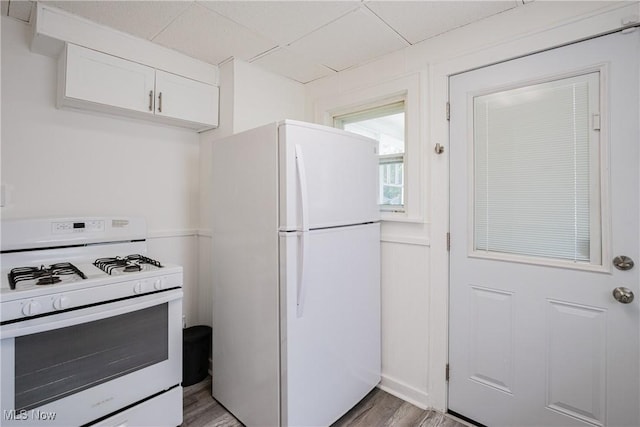 kitchen with a paneled ceiling, white appliances, white cabinets, and light wood-style flooring