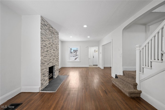 unfurnished living room with baseboards, visible vents, stairway, dark wood-style flooring, and a fireplace