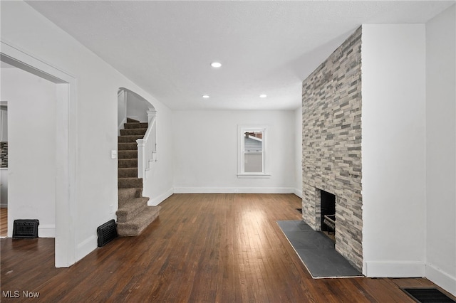 unfurnished living room featuring dark wood-style flooring, a fireplace, visible vents, baseboards, and stairway