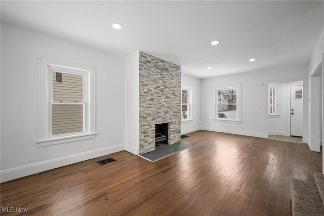 unfurnished living room featuring dark wood-style flooring, a fireplace, visible vents, and baseboards