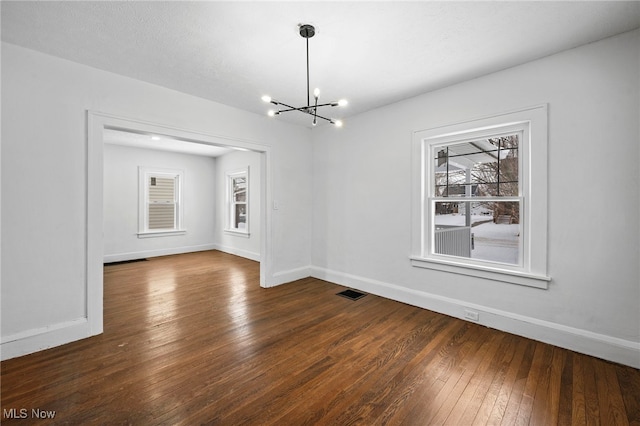 empty room with dark wood-style floors, a chandelier, visible vents, and baseboards