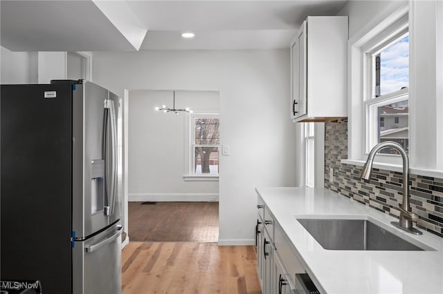 kitchen with light countertops, light wood-style flooring, white cabinetry, a sink, and stainless steel fridge