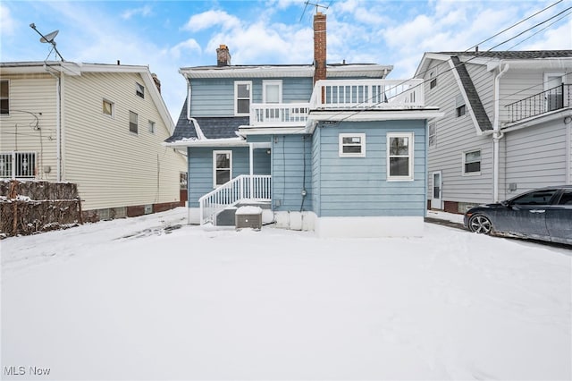 snow covered back of property featuring a chimney and a balcony