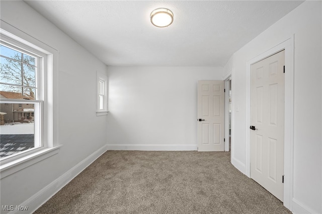 spare room with carpet, a textured ceiling, and baseboards
