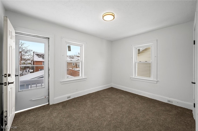 empty room with a textured ceiling, dark colored carpet, and baseboards