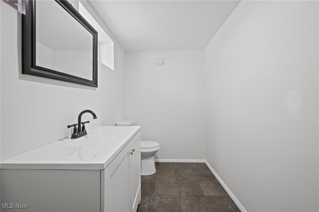 bathroom with toilet, stone finish flooring, vanity, and baseboards