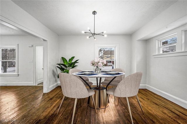 dining room featuring dark wood-type flooring, a chandelier, a textured ceiling, and baseboards