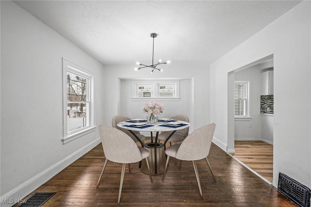 dining room with dark wood-style flooring, visible vents, a notable chandelier, and baseboards