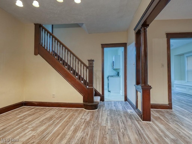 entrance foyer featuring a textured ceiling, baseboards, stairway, light wood-type flooring, and decorative columns