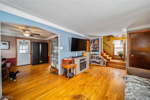 living area with stairs, arched walkways, a ceiling fan, and light wood-style floors