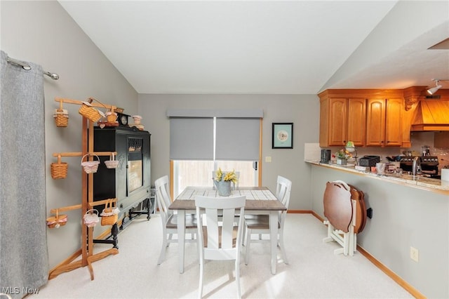 dining space with vaulted ceiling, baseboards, and light colored carpet