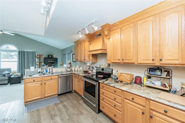 kitchen featuring premium range hood, a sink, vaulted ceiling, appliances with stainless steel finishes, and light wood finished floors