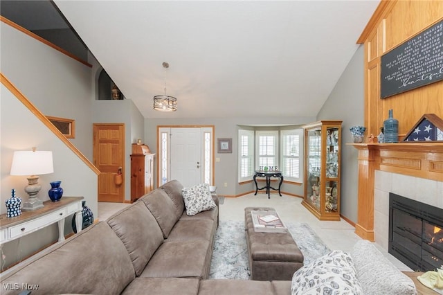 living area featuring light colored carpet, high vaulted ceiling, a tile fireplace, baseboards, and stairs