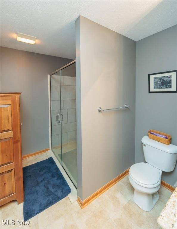 bathroom featuring a textured ceiling, a stall shower, toilet, and baseboards