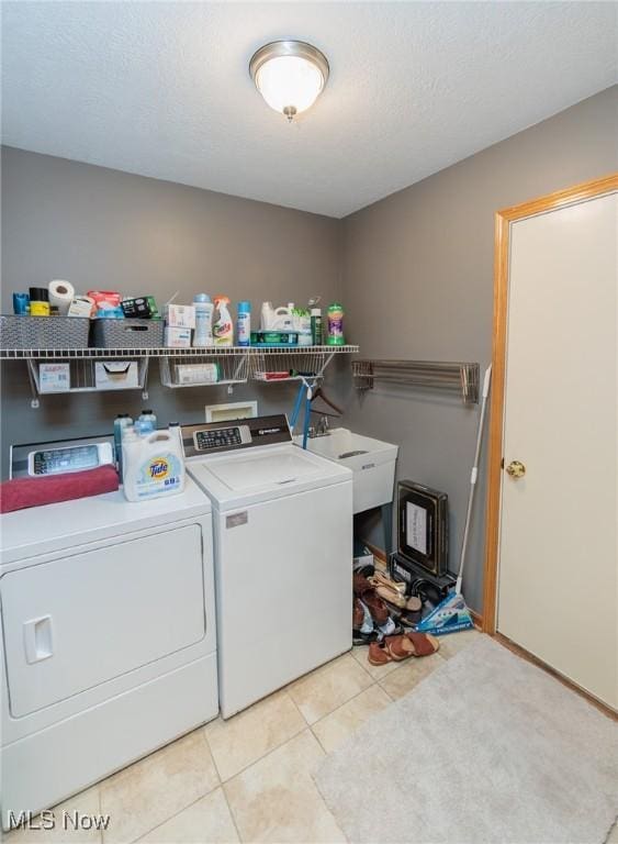 washroom with light tile patterned floors, a sink, a textured ceiling, separate washer and dryer, and laundry area